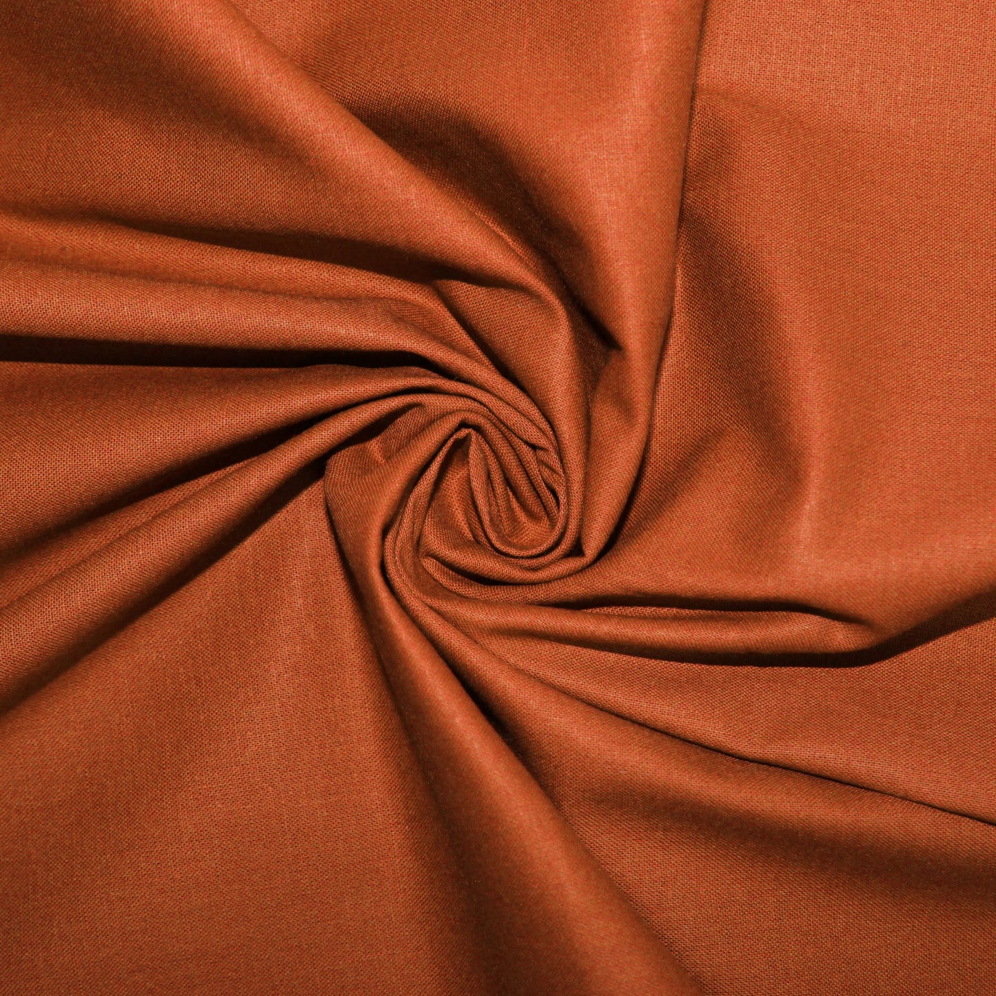 A close-up of draped rust-orange fabric arranged in a spiral pattern, showing its smooth texture and color.