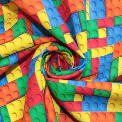 A close-up of colorful fabric printed with a repeating pattern of toy building-block squares in red, orange, yellow, green, and blue, arranged in a spiral drape.