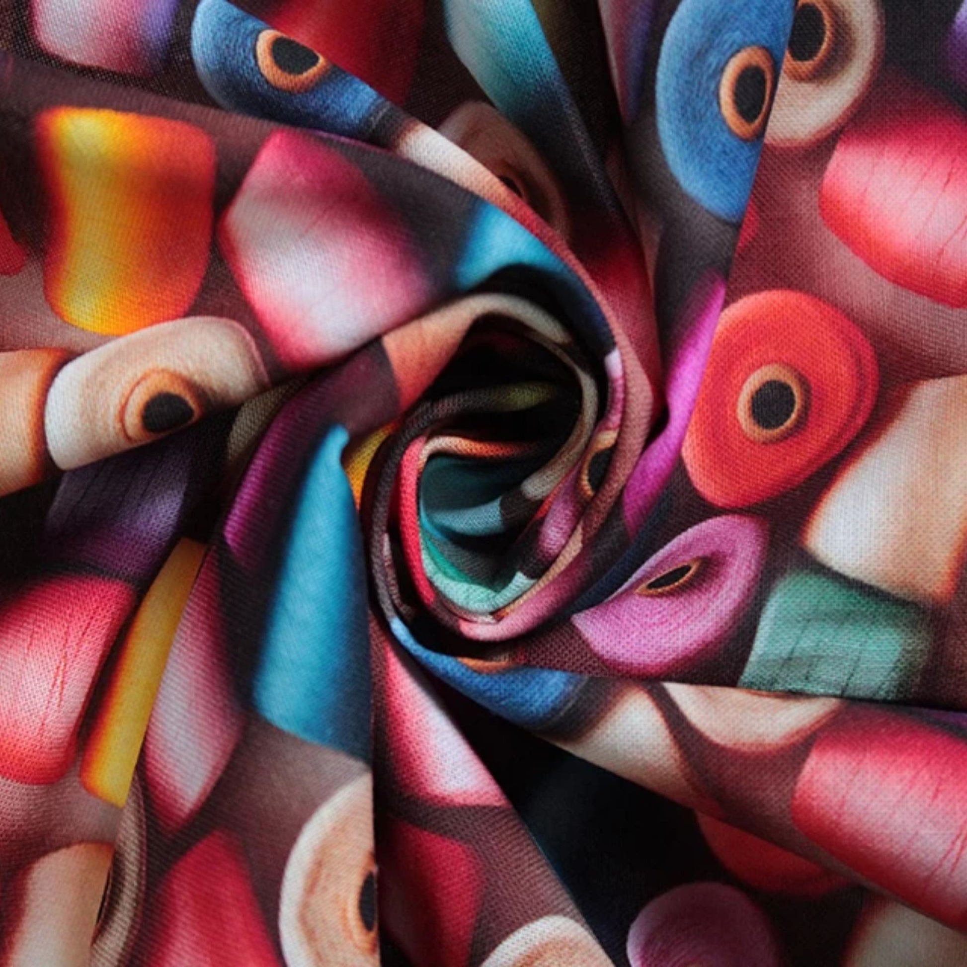 A close-up of a multicolored printed fabric arranged in a spiral twist, showing an abstract pattern with red, pink, blue, purple, yellow, and beige shapes.