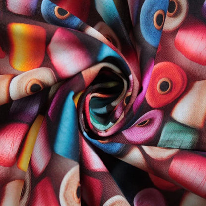 A close-up of a multicolored printed fabric arranged in a spiral twist, showing an abstract pattern with red, pink, blue, purple, yellow, and beige shapes.