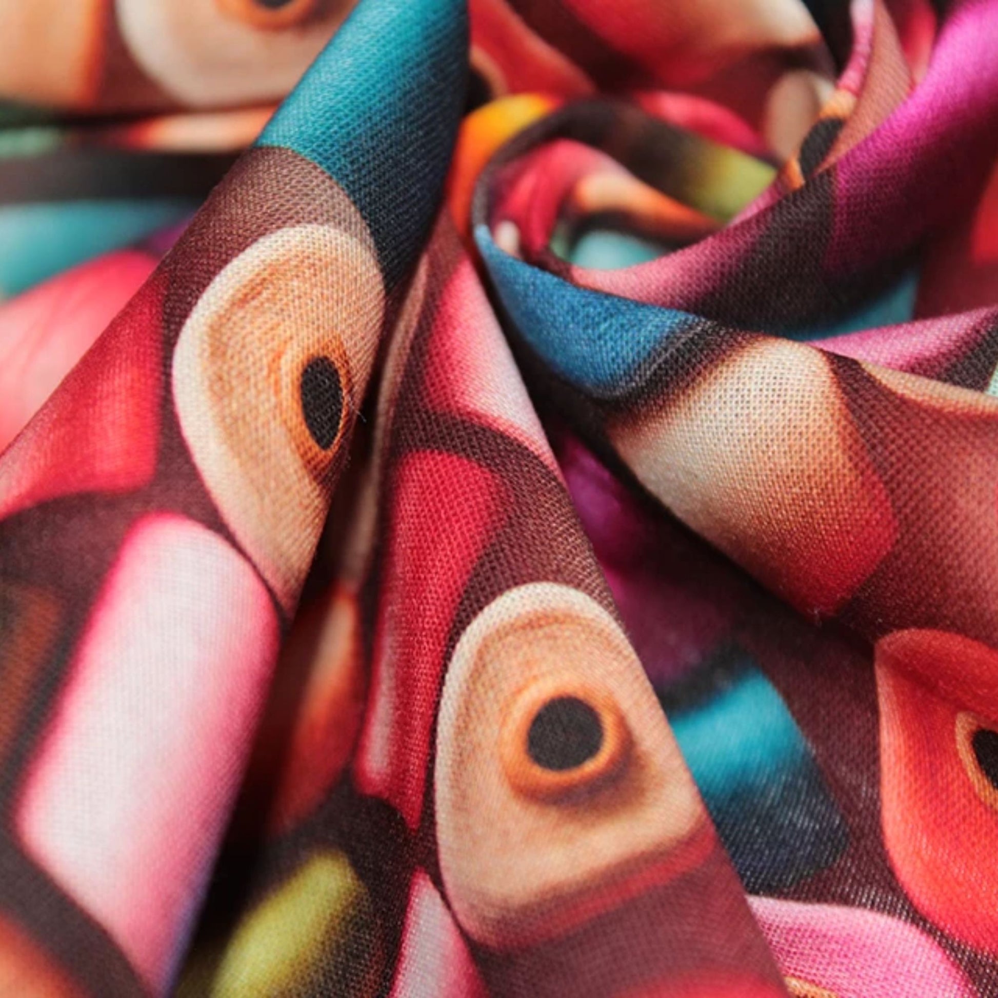 A close-up of a draped fabric with a colorful abstract print featuring stylized eyes in shades of pink, red, teal, beige, and brown.